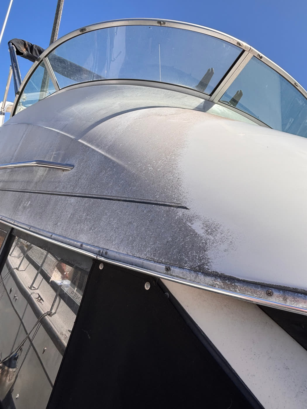 Heavily oxidized gelcoat on a boat bow, half cut back to a clean white finish
